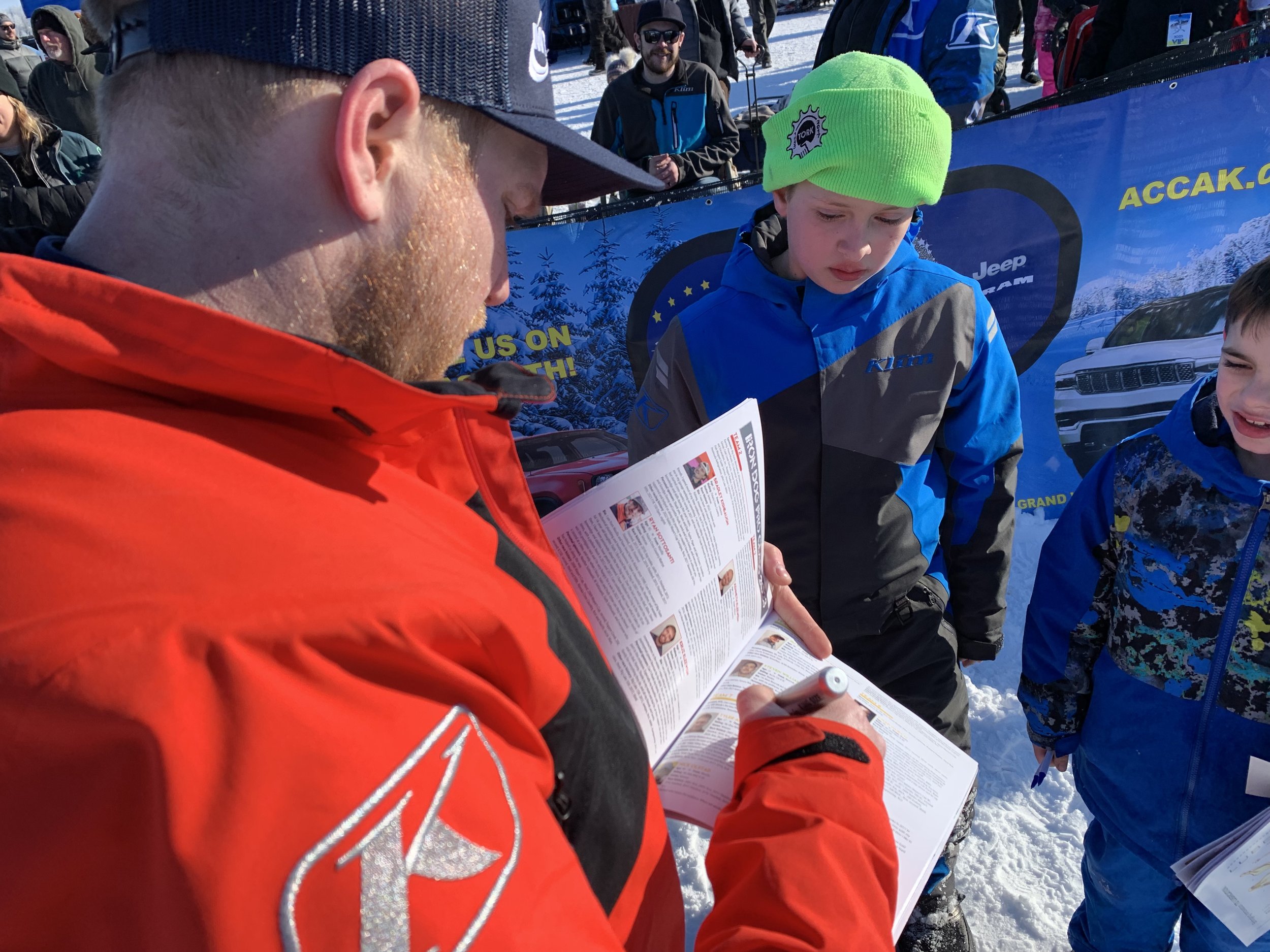 Team 7’s Tyler Aklestad signs the 2023 Iron Dog Official Guide for young race fans. This is Aklestad’s fourth Iron Dog Victory, and third one with partner Nick Olstad. Iron Dog photo